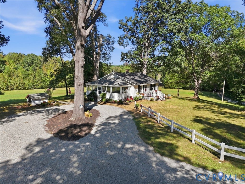 White exterior siding, screened porch, gravel driveway, white post-and-rail fencing, and mature trees.