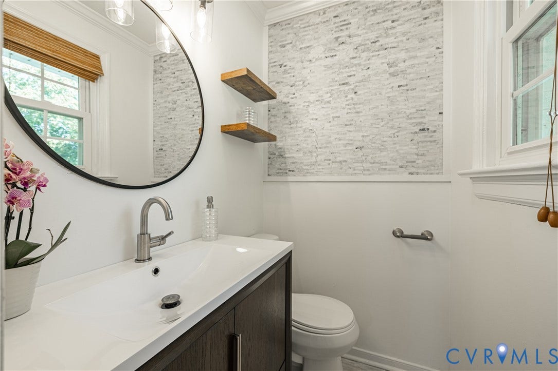 5312 Marian Street, Richmond, VA 23226 Integrated sink and countertop, dark wood-finish vanity, circular wall mirror, accent wall with stacked stone, and recessed lighting