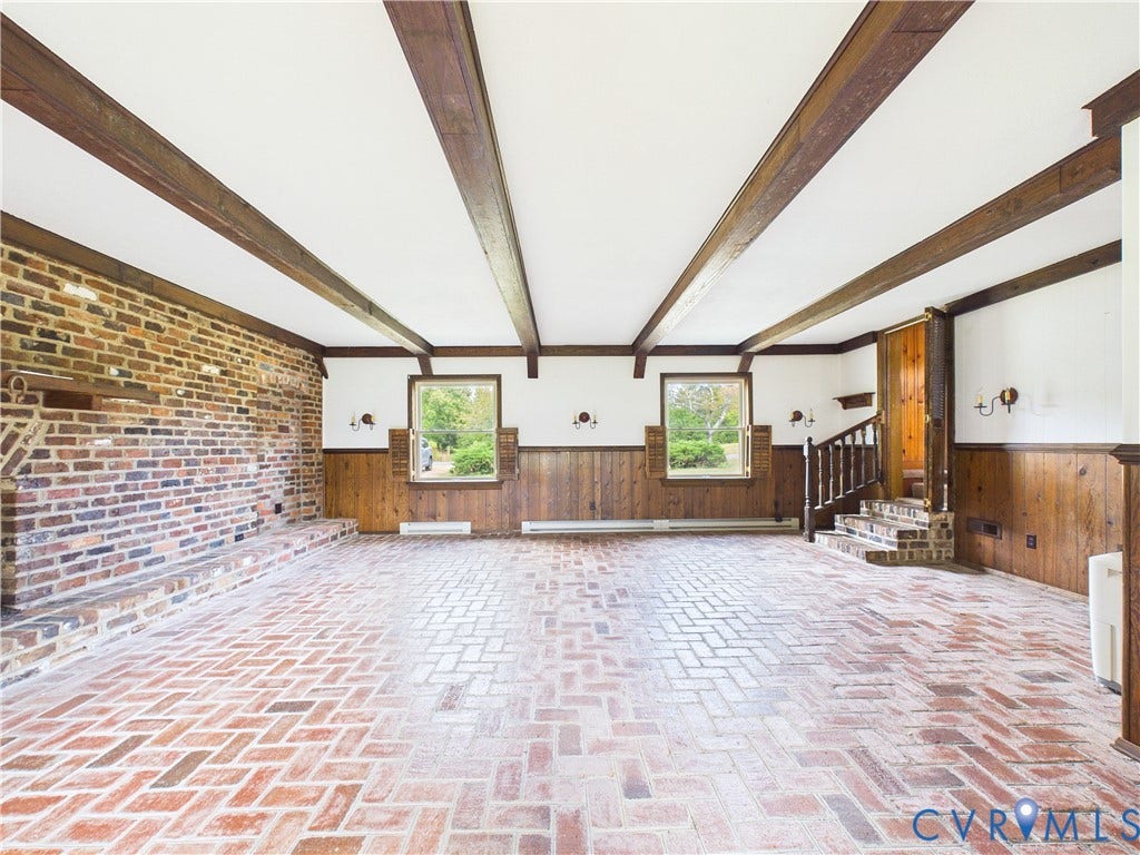 Herringbone brick flooring, exposed ceiling beams, brick accent wall, wood paneling, and a built-in brick hearth