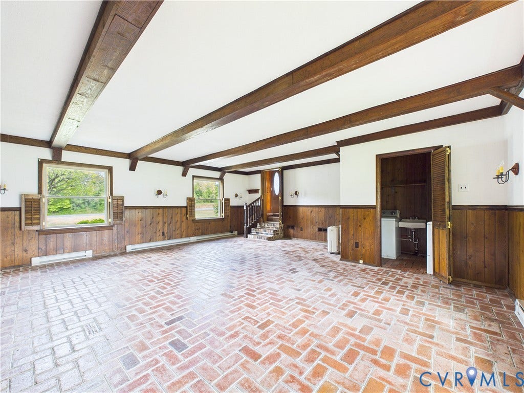 Exposed wood beams, brick flooring, wood paneling, multiple windows, and a utility sink