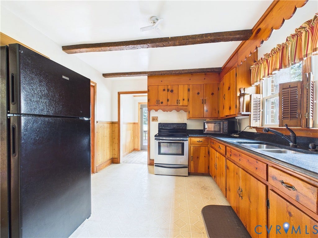 Kitchen featuring wood cabinetry, dark countertops, a double basin sink, and exposed ceiling beams