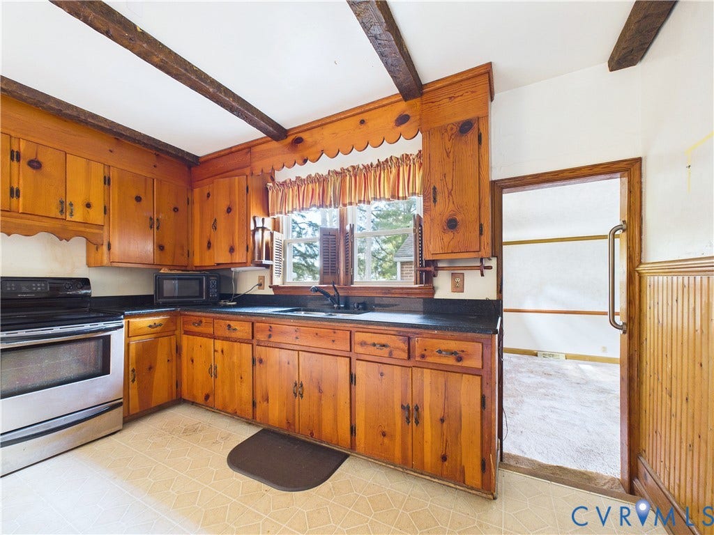 Kitchen featuring exposed wood ceiling beams, wood cabinetry, a stainless steel range, a window, and beadboard paneling