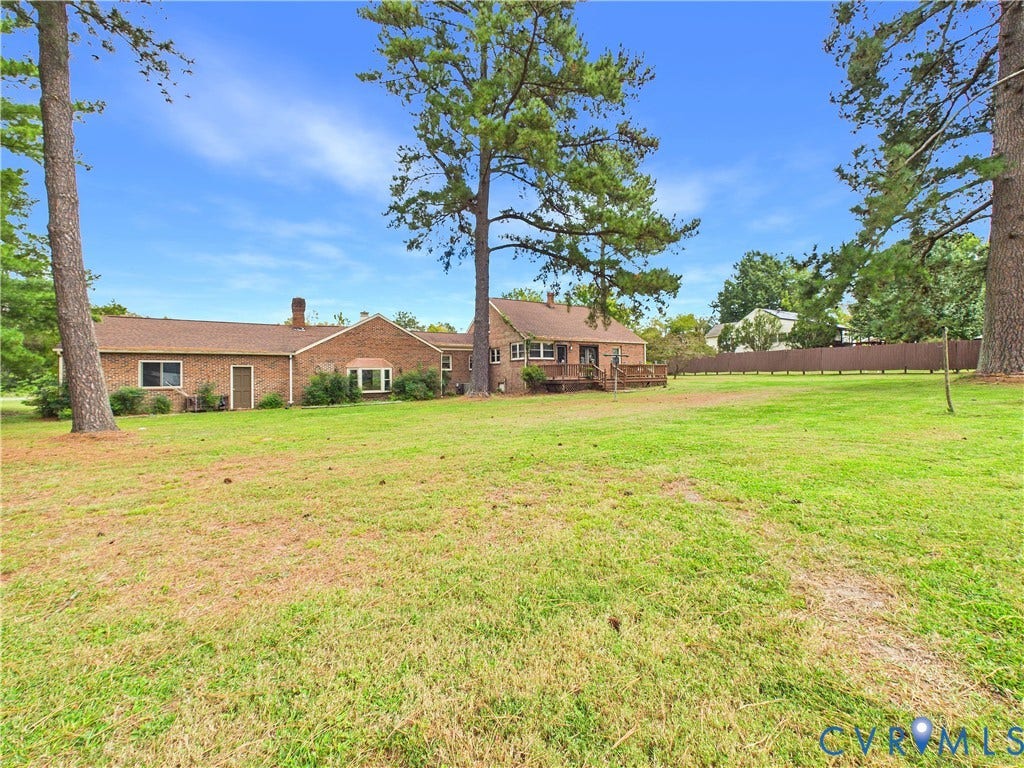 Expansive grassy yard with mature trees, a brick exterior, and a wood deck