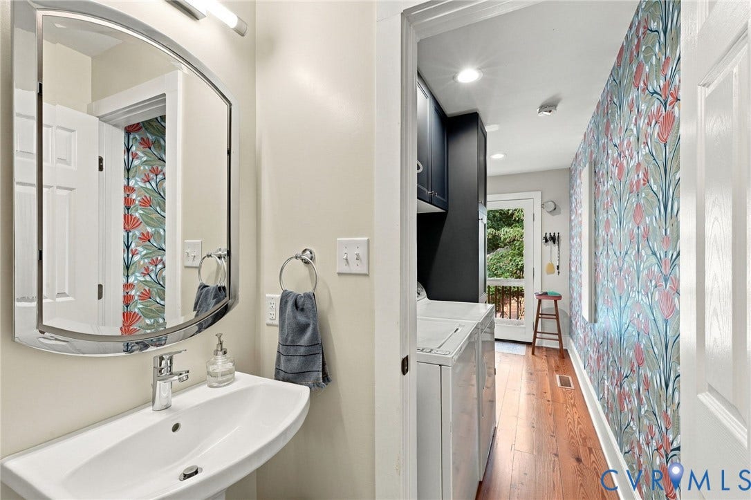 Pedestal sink with chrome faucet, curved wall mirror, built-in dark cabinetry, recessed lighting, and wood-finish flooring