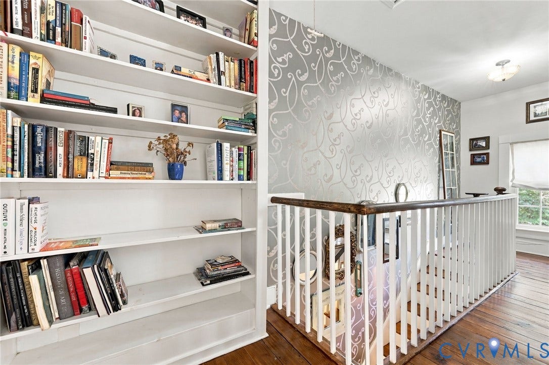 Built-in shelving, wood-finish flooring, decorative wall covering, white balustrade, and a window with natural light