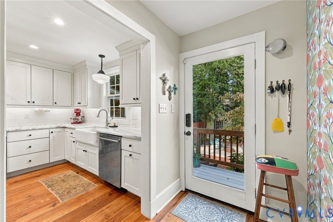 White shaker cabinetry with dark hardware, undermount farmhouse sink, stainless steel dishwasher, light-toned countertop, and wood flooring