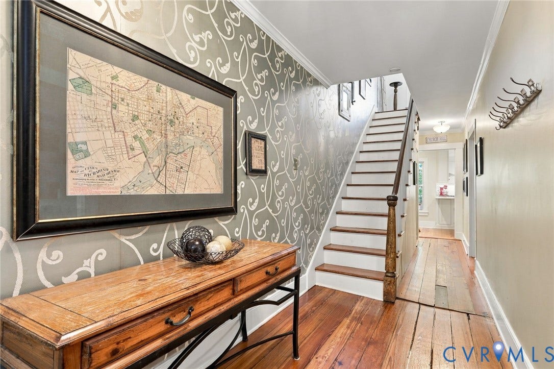 Hardwood flooring, painted risers, staircase with wooden newel post, patterned wallpaper accent wall, and crown molding