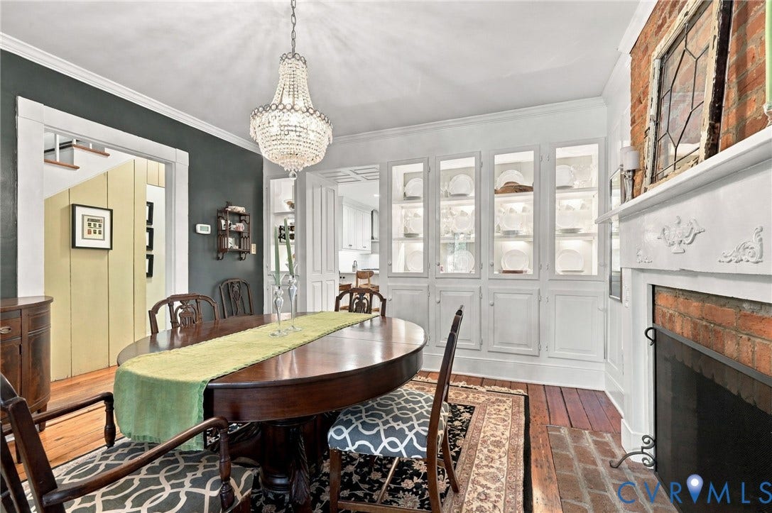 Hardwood flooring throughout, featuring a brick fireplace with a carved mantel, built-in cabinetry with glass-front displays, crown molding, and a crystal chandelier