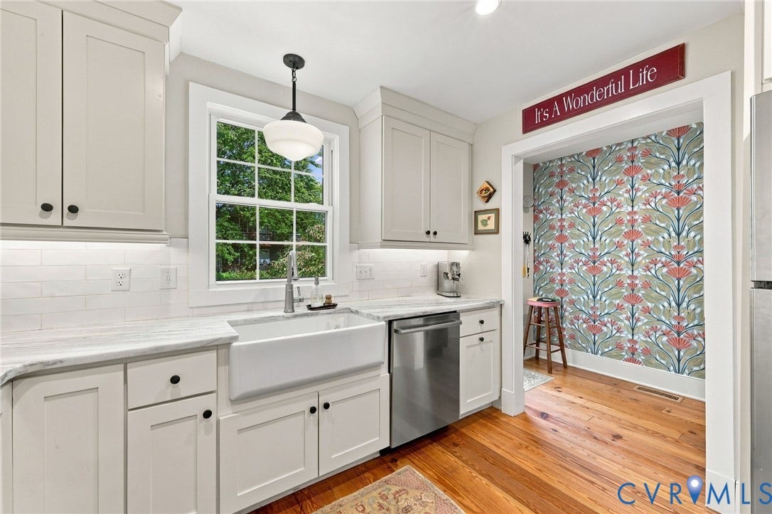 White shaker-style cabinetry with black hardware, farmhouse sink, stainless steel dishwasher, white subway tile backsplash, and light-toned countertops