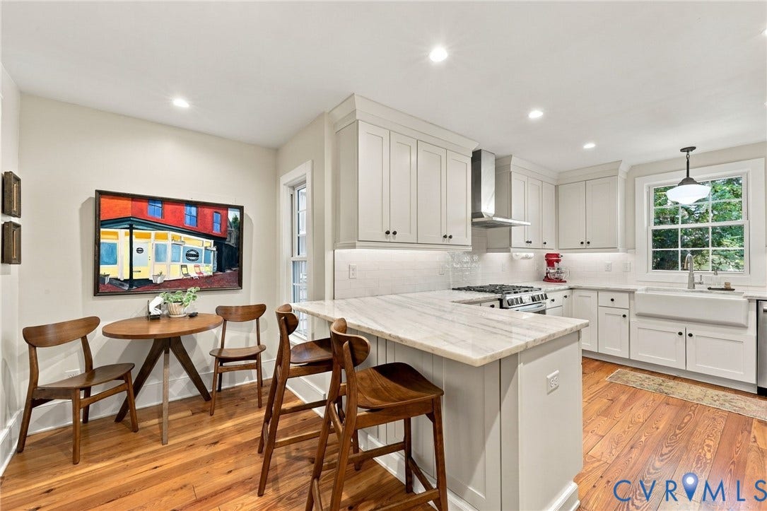 Kitchen featuring wood-finish flooring, white cabinetry, a white farmhouse sink, and an island with a light-toned countertop
