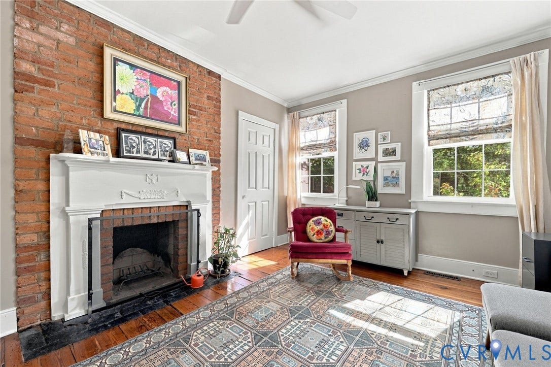 Exposed brick wall featuring a decorative fireplace with a white mantel, wood-finish flooring, and multiple windows