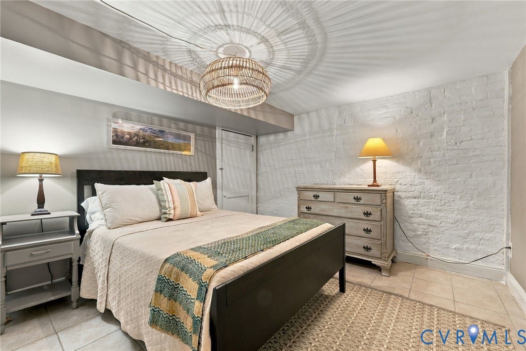 Basement bedroom with woven pendant light fixture, painted brick wall, tile flooring, and a built-in door