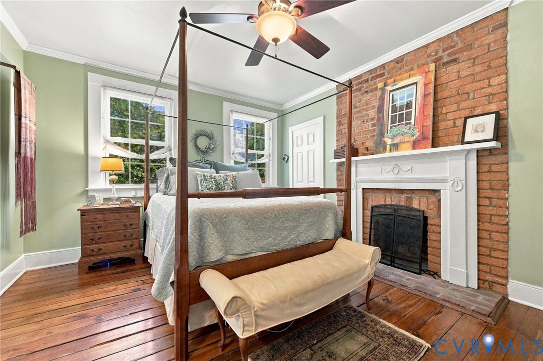 Exposed brick accent wall with a white mantelpiece, hardwood flooring, and a ceiling fan with integrated lighting