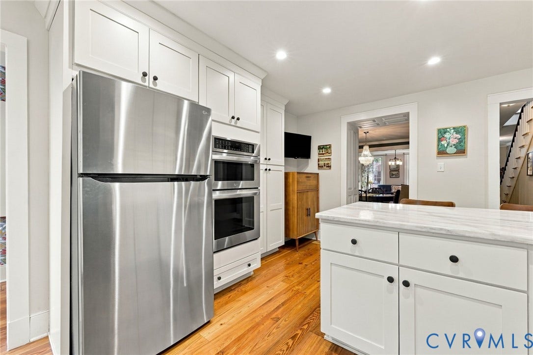Integrated stainless steel refrigerator and double oven, white shaker cabinetry with black hardware, white stone countertop, recessed lighting, and wood-finish flooring