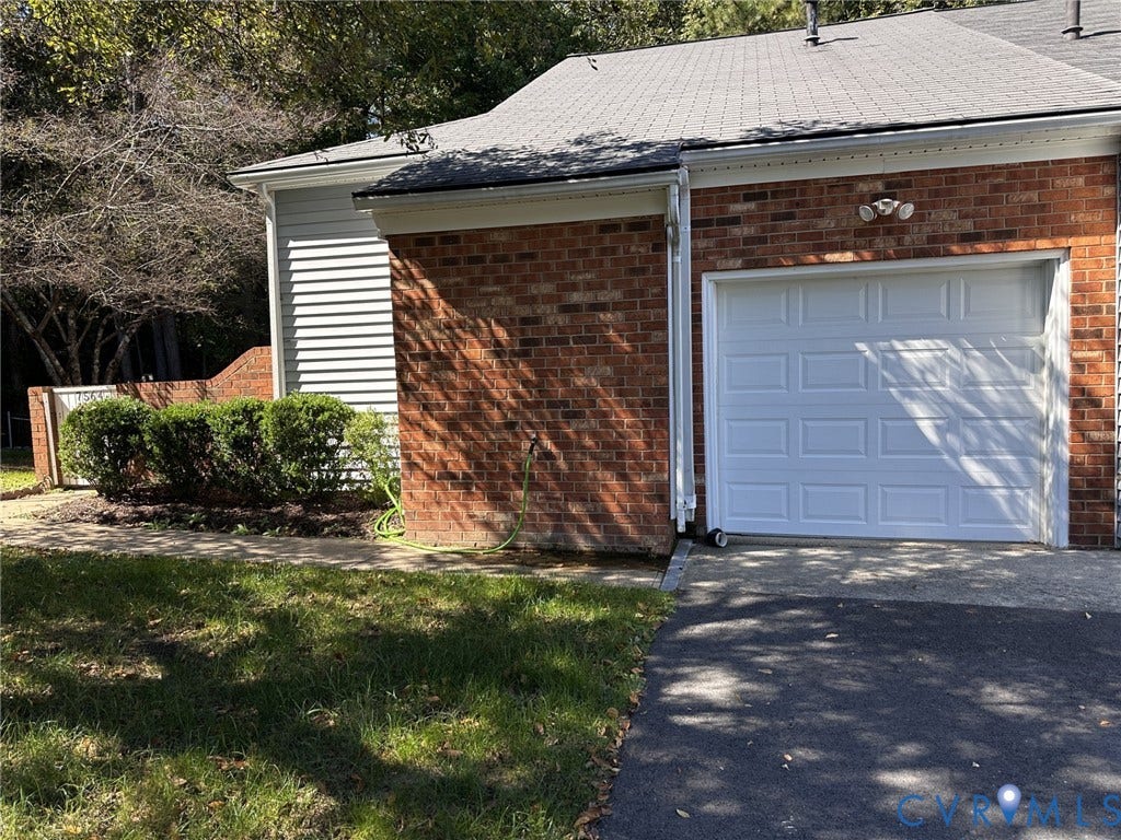 Brick exterior with light siding, a white panel garage door, dark shingle roof, and established shrubs