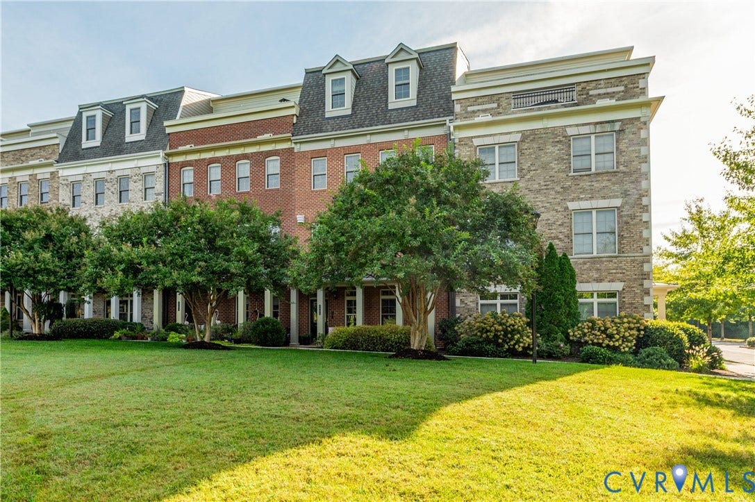 Stone and brick facade townhomes featuring dormer windows, individual porticos with columns, and surrounding manicured landscaping