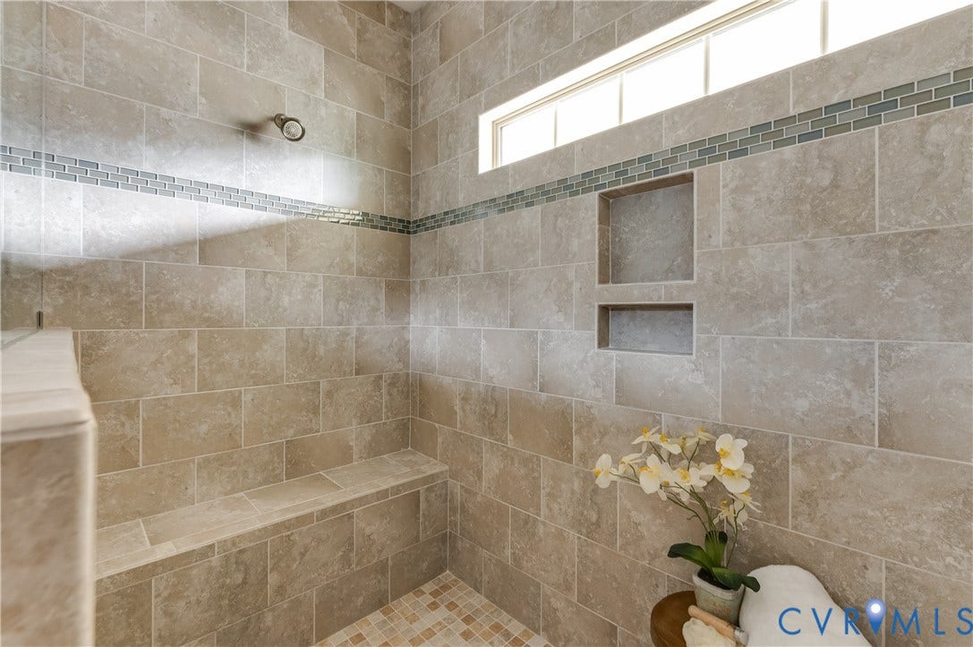 Tiled shower with a glass block transom window, decorative tile accent band, recessed shelving, a built-in bench, and mosaic tile flooring
