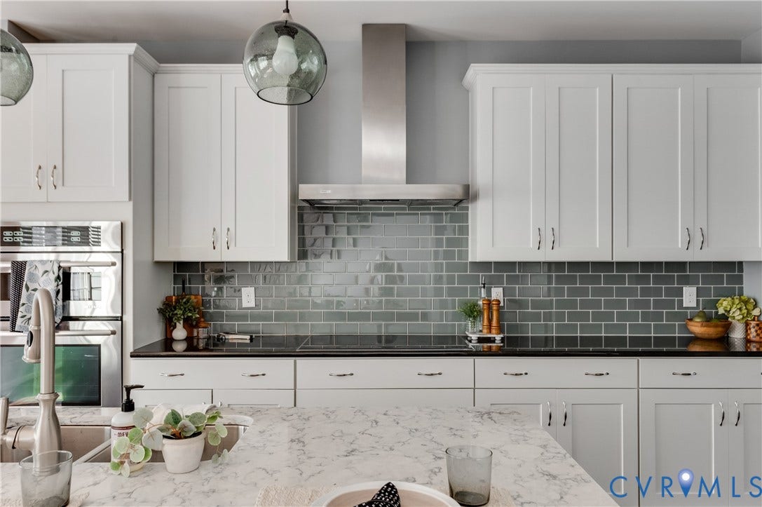 White shaker-style cabinetry, stainless steel double wall ovens, glass subway tile backsplash, black countertops, and a white marble-finish island
