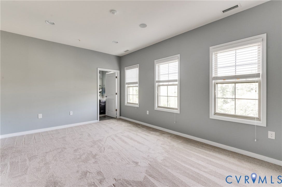Light gray wall paint, recessed lighting, two windows with white blinds, and a light-colored carpeted floor