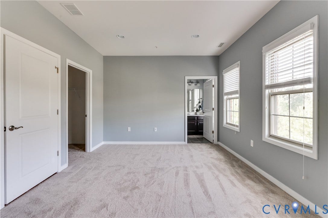 Spacious room with light-colored carpeting, two windows with blinds, and white trim