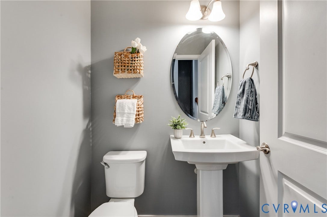 Pedestal sink with brushed nickel faucet, wall-mounted oval mirror, and overhead vanity lighting
