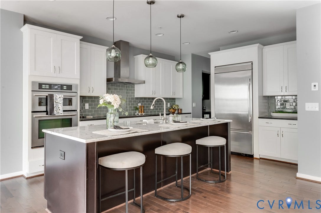 Kitchen featuring a center island with seating, white shaker-style cabinetry, stainless steel appliances, a tile backsplash, and wood-finish flooring