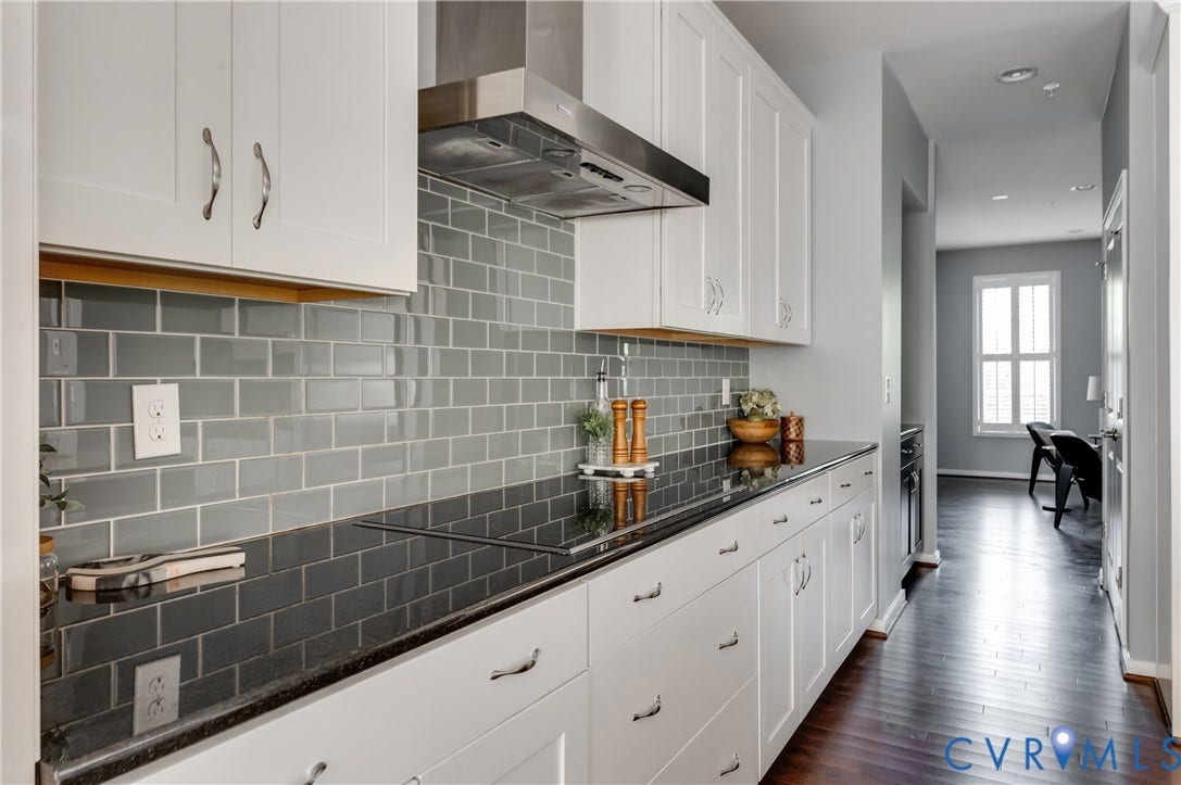 Galley kitchen featuring white cabinetry, a subway tile backsplash, dark countertops, and stainless steel appliances