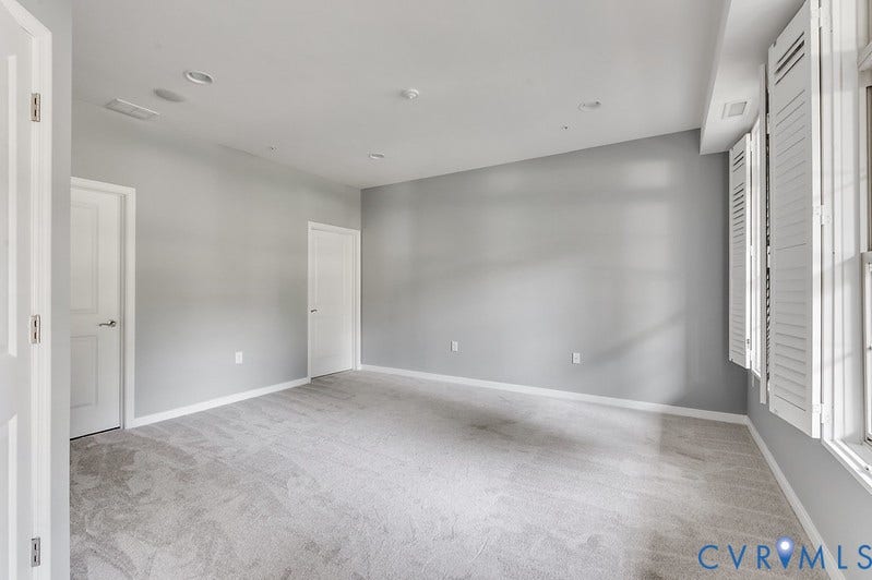 Neutral grey wall paint, grey carpet flooring, recessed ceiling lighting, white interior doors, and white window shutters