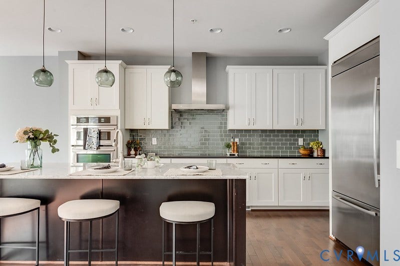 Kitchen featuring a large island with a light-toned countertop, white cabinetry with dark hardware, stainless steel appliances, a subway tile backsplash, and wood-finish flooring