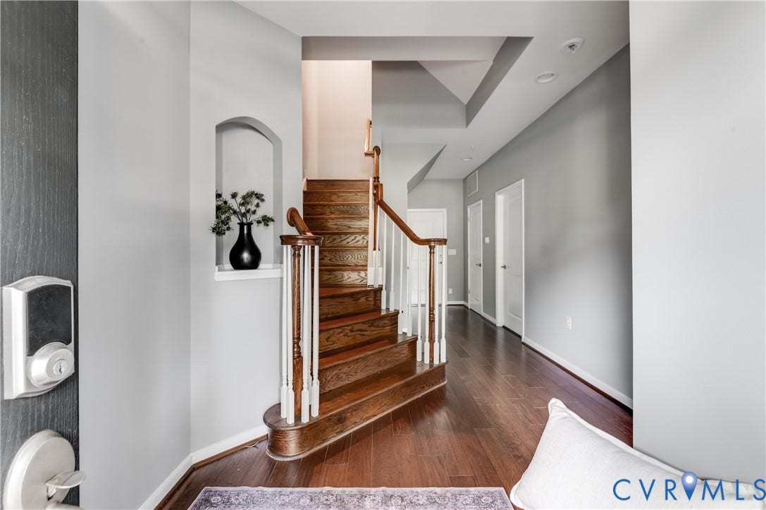 Hardwood flooring, curved staircase with wood banister, built-in wall niche, recessed lighting, and tray ceiling detail