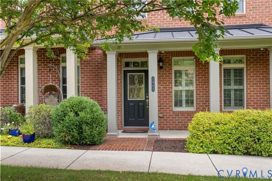 Brick facade with a covered entry, white columns, a black front door with decorative glass, and window shutters