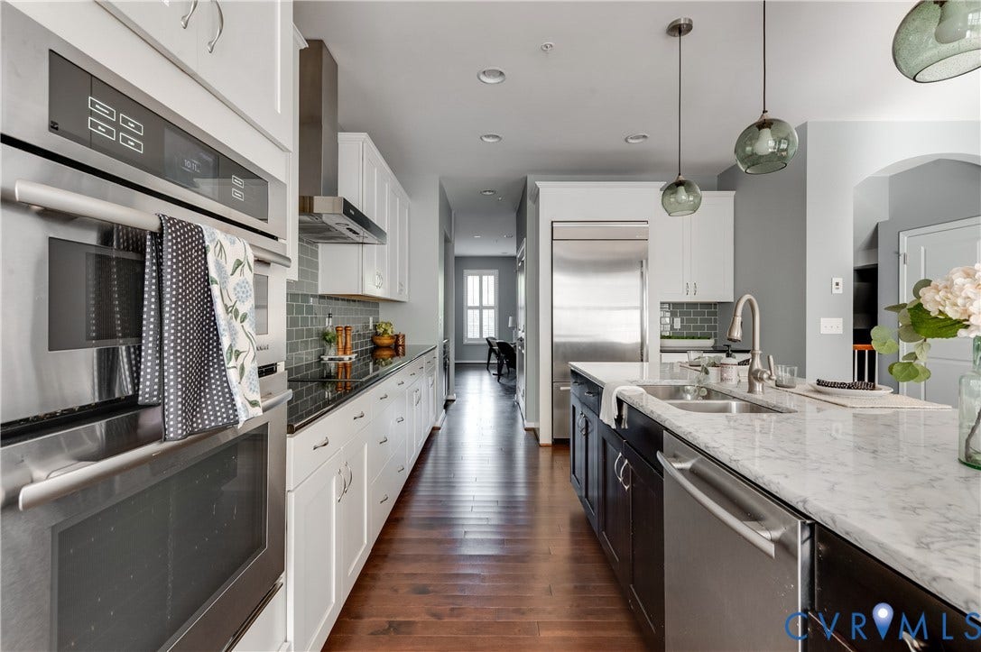 Gourmet kitchen with stainless steel appliances, custom cabinetry, marble island, wood-finish flooring, and pendant lighting