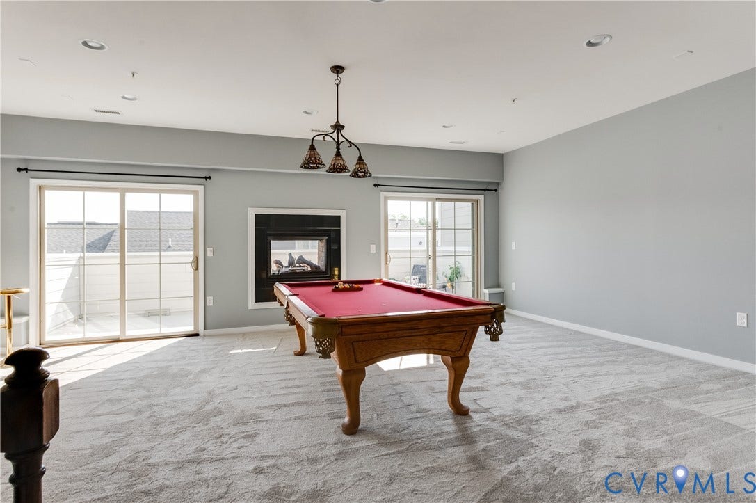 Spacious room featuring light gray walls, light-colored patterned carpeting, a centered ceiling light fixture, and recessed lighting