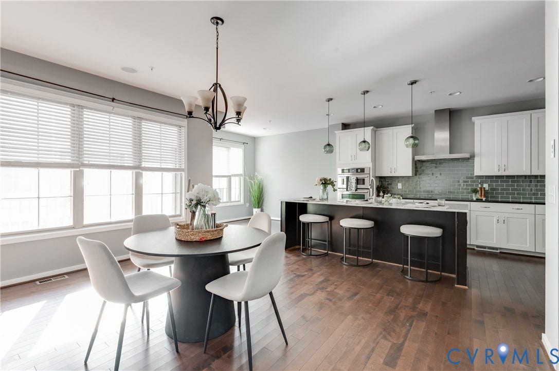 Open-concept design featuring wood-finish flooring, a kitchen island with seating, pendant lighting, a tile backsplash, and a dining area with a chandelier