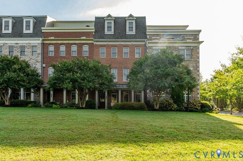 Traditional facade featuring brick and stone cladding, dormer windows, a manicured lawn, mature trees, and covered entryways with columns