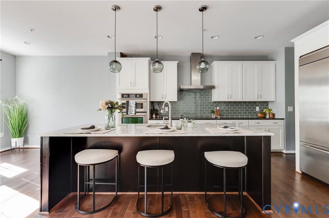 Kitchen featuring an expansive island with a light-colored countertop, white shaker-style cabinetry, stainless steel appliances, a subway tile backsplash, and wood-finish flooring