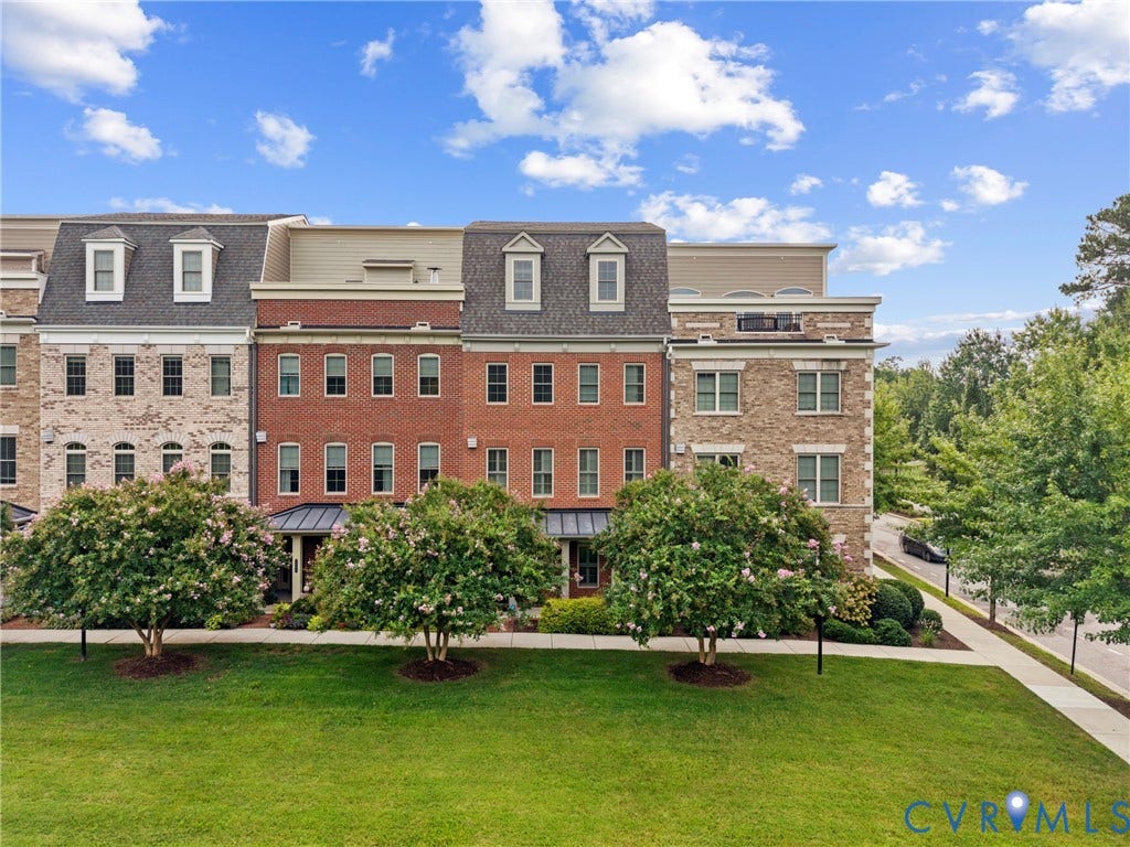 Brick and stone facade townhome with dormer windows, a manicured lawn, and mature trees