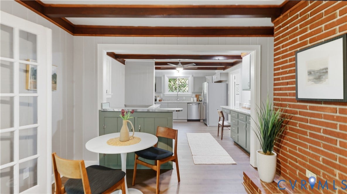 Exposed brick wall, wood-finish flooring, wood beam ceiling, white paneling, and a kitchen with light green cabinetry