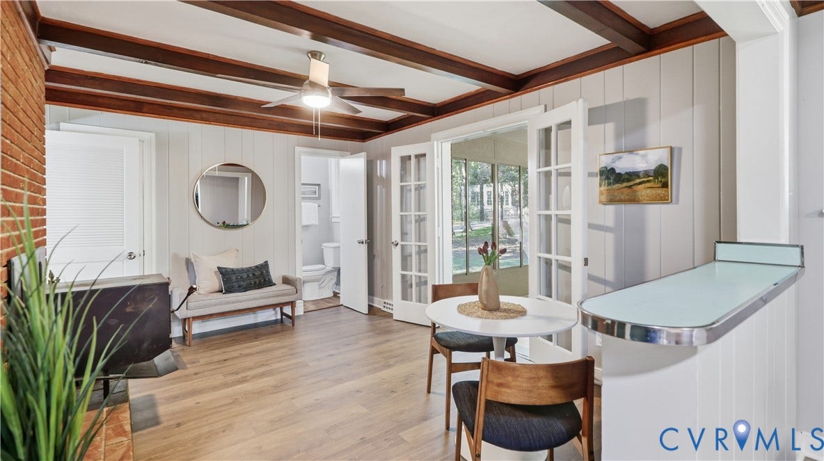 Exposed wood beam ceiling, wood-finish flooring, brick fireplace, wall paneling, and French doors