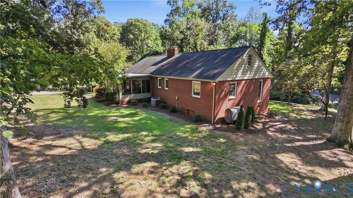 Brick exterior with a screened porch, large yard, mature trees, and a sloped terrain