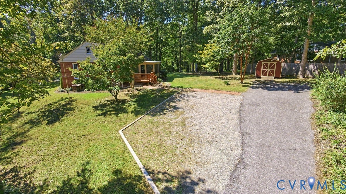 Brick exterior with an attached screened porch, gravel parking area, paved driveway, and a detached storage shed