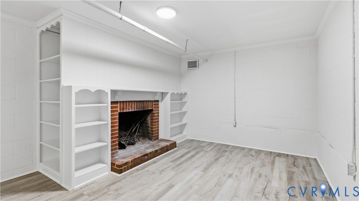 Brick fireplace with hearth, built-in shelving, wood-finish flooring, and recessed ceiling light