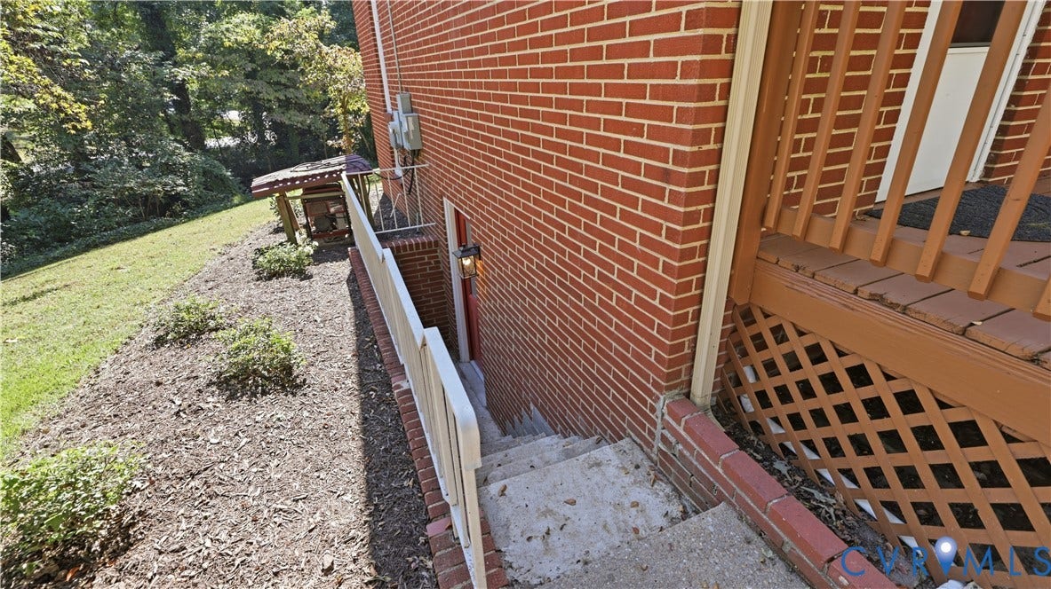 Red brick exterior with concrete steps, white handrail, and exterior lighting