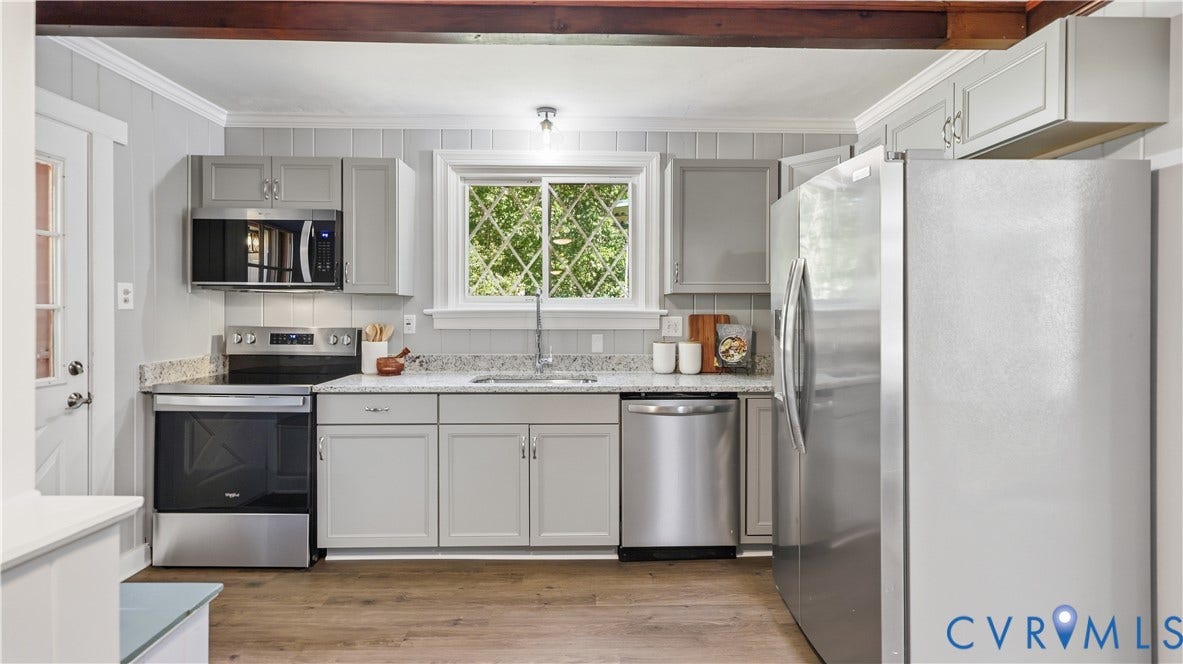 Modern kitchen featuring light gray cabinetry, stainless steel appliances, wood-finish flooring, granite-style countertops, and a diamond-pane window