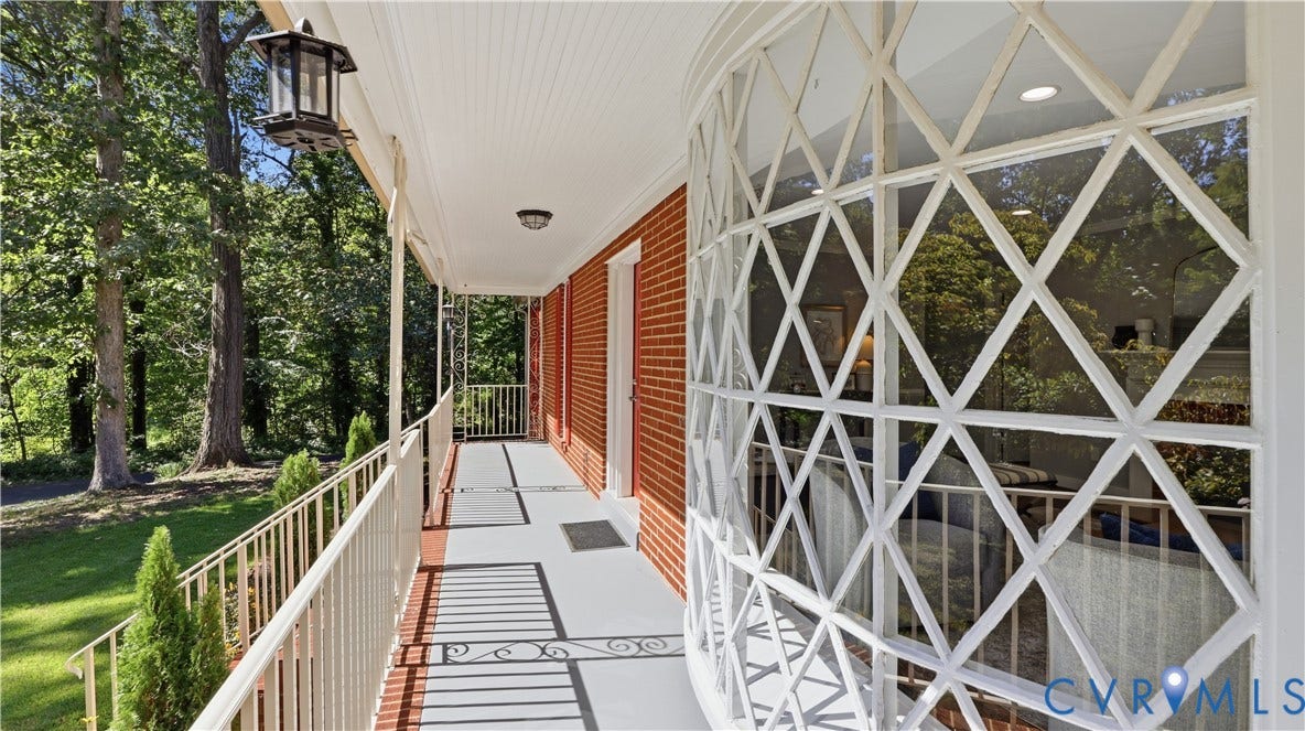 Brick facade, decorative bay window with diamond-patterned muntins, covered porch with white railing, beadboard ceiling, and exterior lighting fixture