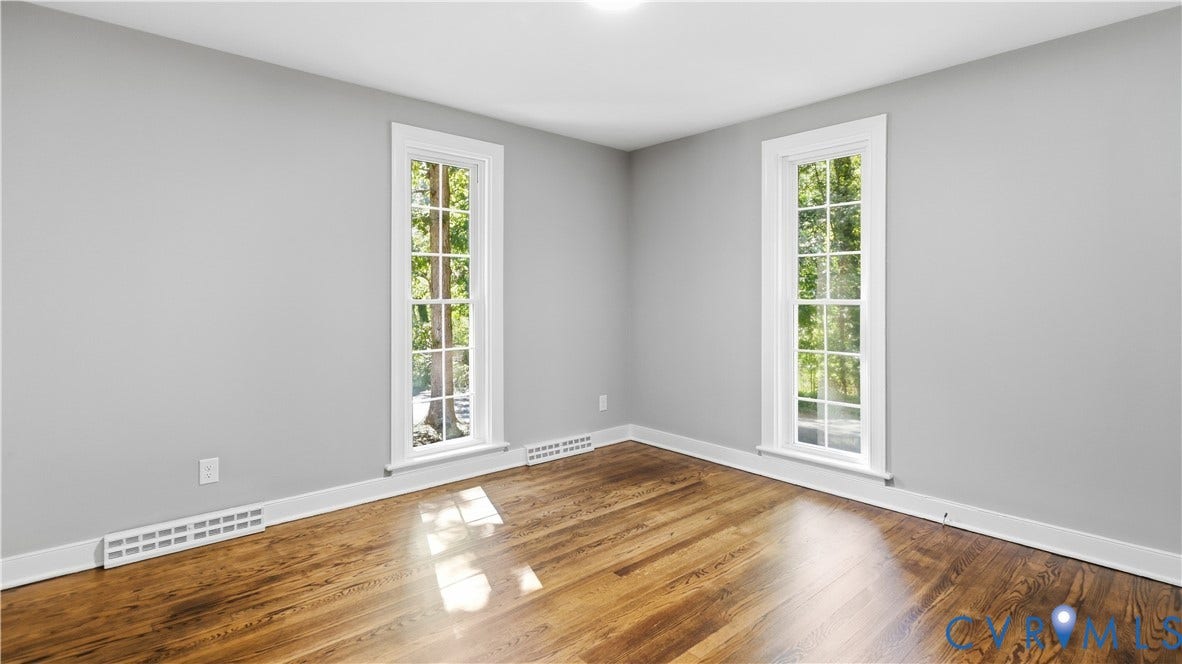 Hardwood flooring throughout, neutral wall tones, and tall windows with bright white trim