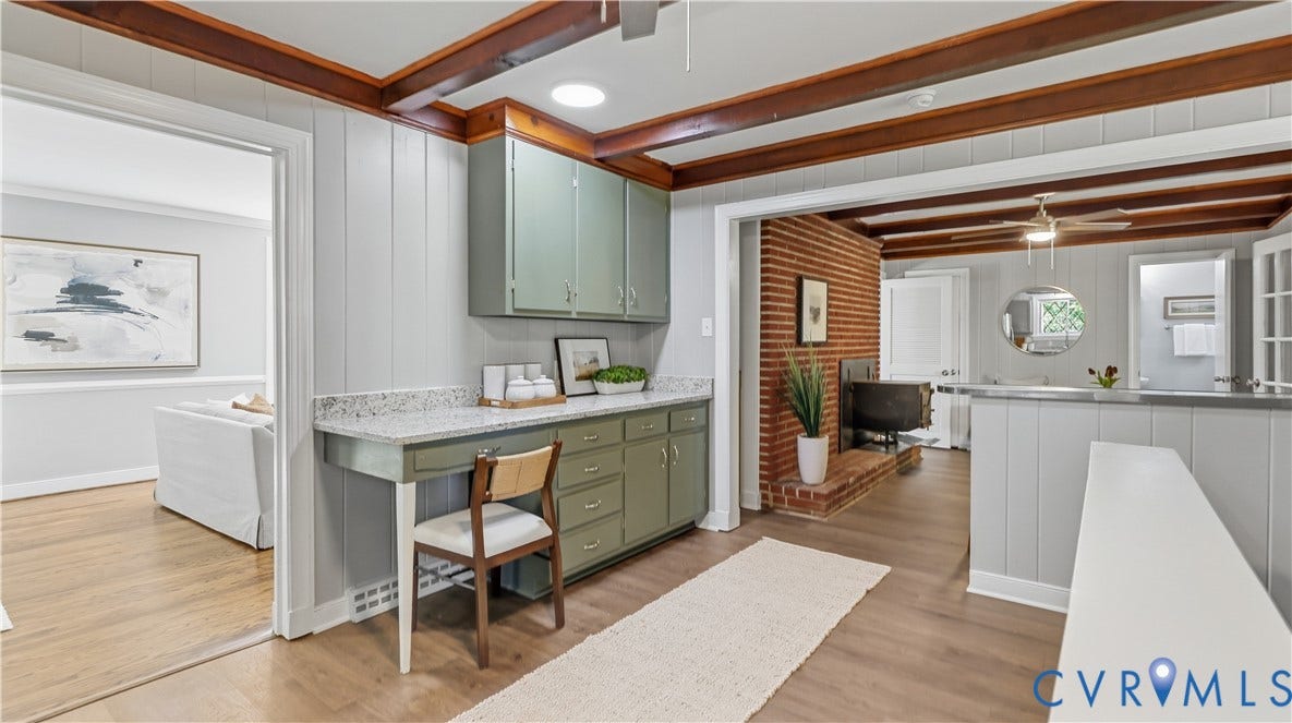 Wood-finish flooring throughout, exposed wood beam ceiling, built-in cabinetry with a stone-finish countertop, brick fireplace, and paneling accents