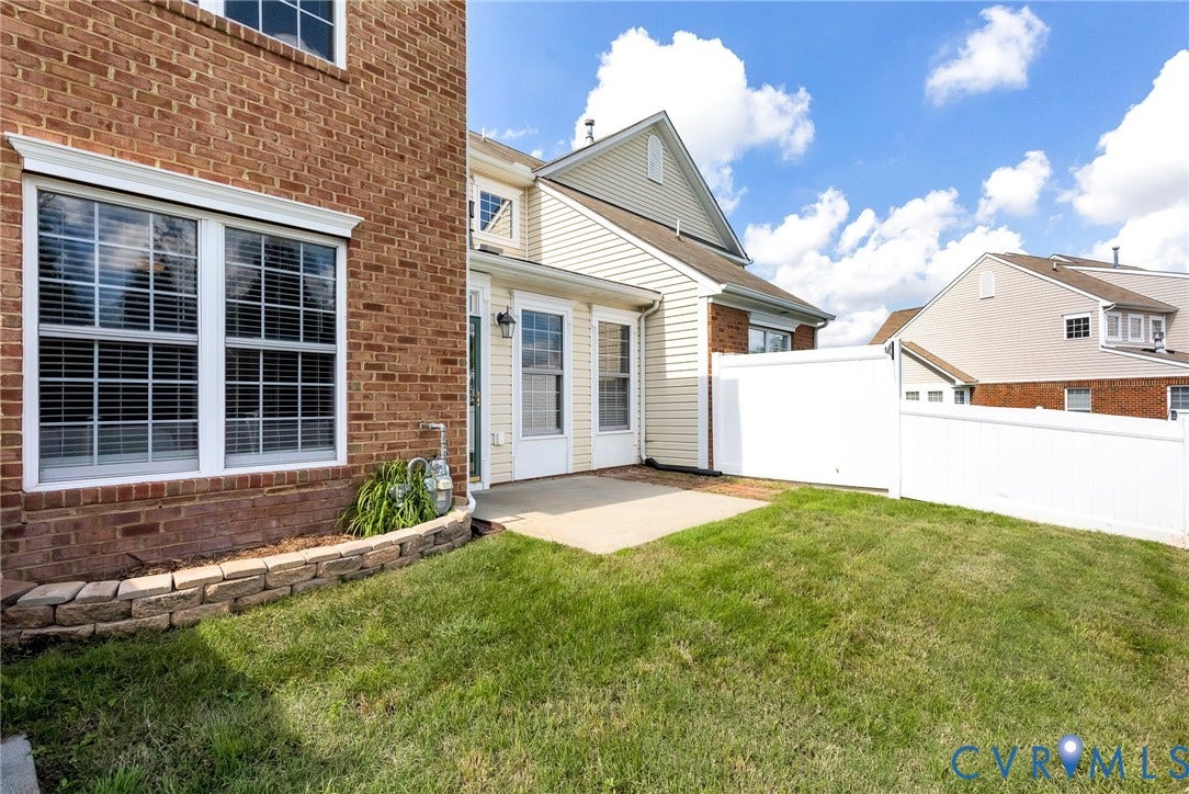 7728 Marshall Arch Drive, Liberty Trace, Mechanicsville, VA 23111 Brick and siding exterior, white vinyl fencing, concrete patio, stone retaining wall, and manicured lawn