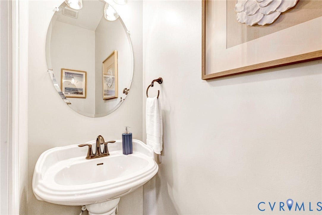 7728 Marshall Arch Drive, Liberty Trace, Mechanicsville, VA 23111 Pedestal sink with bronze-finish faucet, oval mirror with overhead sconce lighting, and a coordinating bronze-finish towel ring