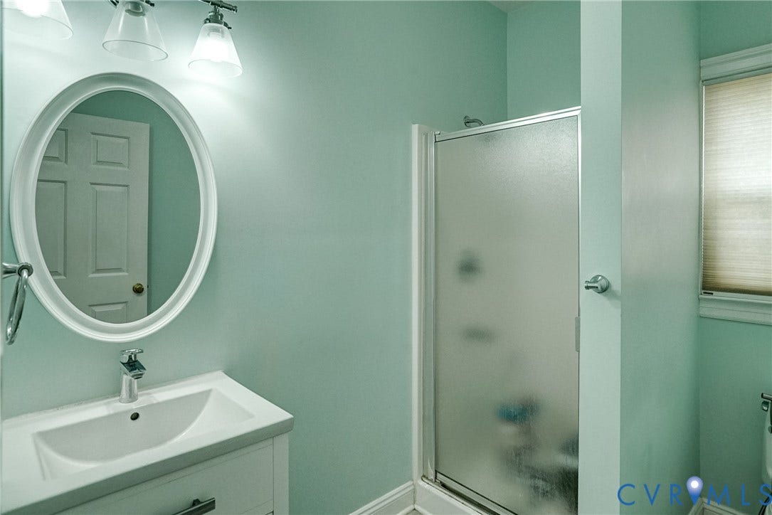 8805 Eli Place, Kings Forest, Glen Allen, VA 23060 Vanity with integrated sink, oval framed mirror, glass-enclosed shower, window with privacy blind, and wall-mounted light fixture